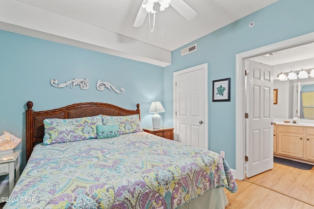 bedroom featuring a textured ceiling, ensuite bathroom, light wood-type flooring, and ceiling fan