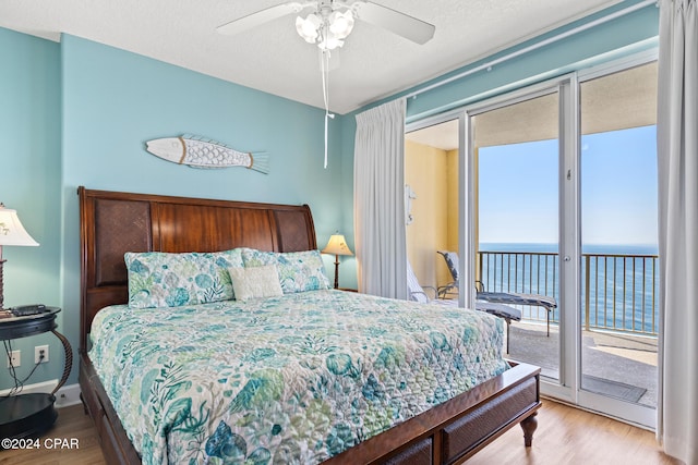 bedroom featuring a water view, light hardwood / wood-style floors, ceiling fan, and access to exterior