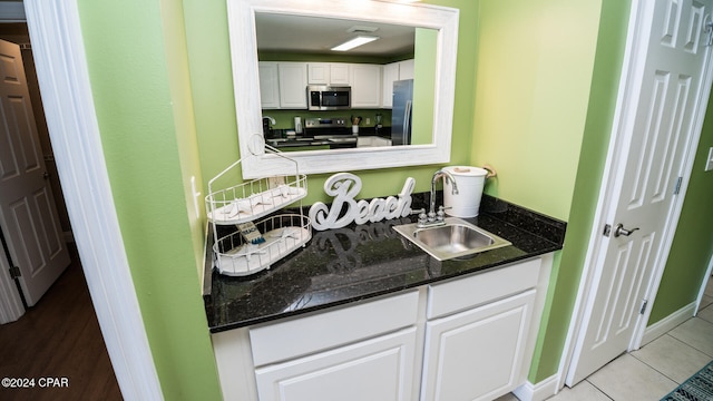 kitchen featuring sink, appliances with stainless steel finishes, dark stone counters, light tile patterned floors, and white cabinets