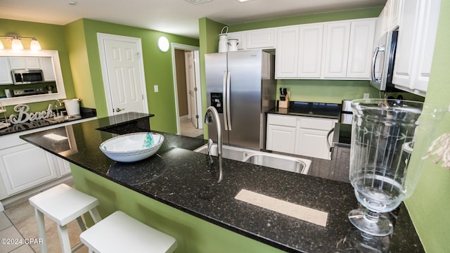 kitchen featuring stainless steel appliances, a breakfast bar area, dark stone counters, and white cabinets