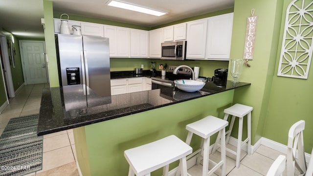 kitchen featuring white cabinetry, kitchen peninsula, appliances with stainless steel finishes, and light tile patterned floors