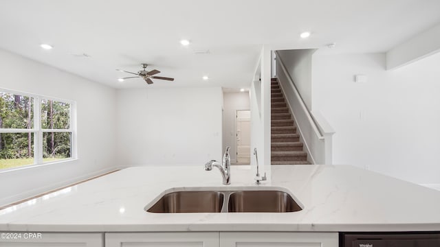 kitchen featuring dishwasher, sink, white cabinets, light stone counters, and ceiling fan