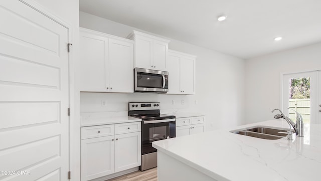 kitchen featuring sink, light stone countertops, white cabinets, light wood-type flooring, and appliances with stainless steel finishes