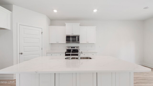 kitchen with a spacious island, light stone counters, appliances with stainless steel finishes, and white cabinetry