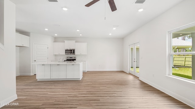 kitchen featuring white cabinets, ceiling fan, appliances with stainless steel finishes, an island with sink, and light hardwood / wood-style floors