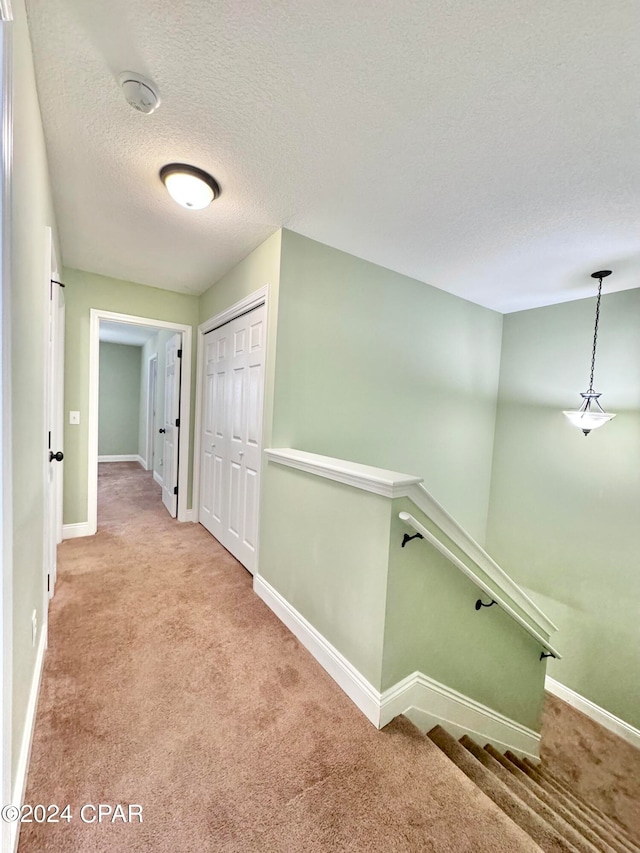 hallway with a textured ceiling and light carpet