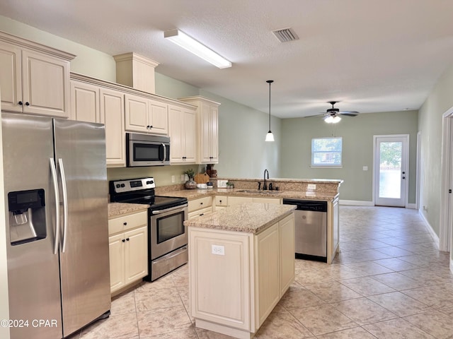 kitchen with kitchen peninsula, stainless steel appliances, sink, cream cabinets, and hanging light fixtures