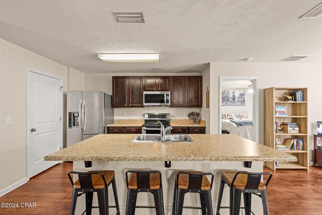 kitchen with stainless steel appliances, dark hardwood / wood-style flooring, a textured ceiling, a breakfast bar area, and a center island with sink