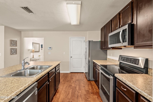 kitchen with sink, stainless steel appliances, light hardwood / wood-style floors, a textured ceiling, and dark brown cabinets