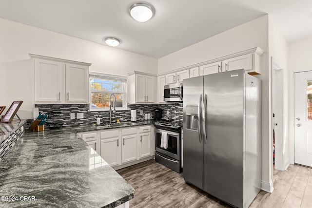 kitchen featuring sink, stainless steel appliances, dark stone counters, white cabinets, and light hardwood / wood-style flooring