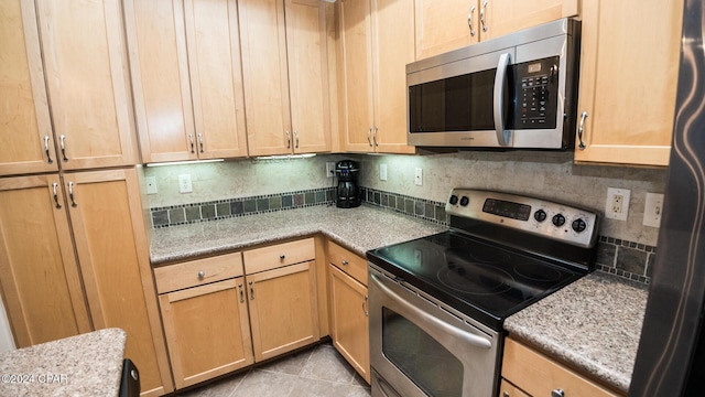 kitchen with light tile patterned floors, stainless steel appliances, backsplash, and light stone countertops