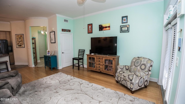 living room featuring light wood finished floors, baseboards, visible vents, and crown molding