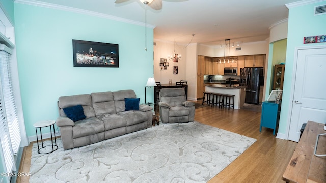 living room featuring crown molding, visible vents, light wood-style flooring, a ceiling fan, and baseboards