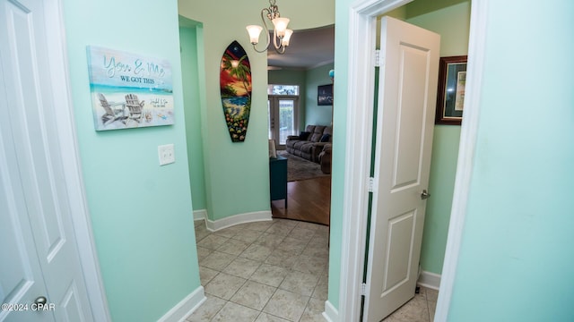 corridor with light tile patterned floors, baseboards, and a chandelier