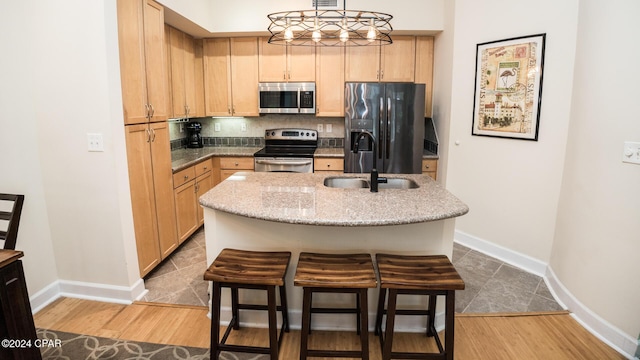 kitchen with pendant lighting, appliances with stainless steel finishes, light brown cabinets, a sink, and an island with sink