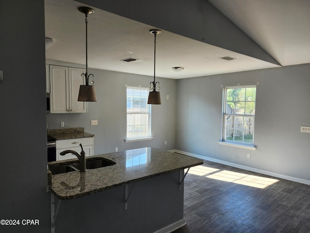 kitchen featuring dark stone counters, a kitchen breakfast bar, hanging light fixtures, vaulted ceiling, and dark hardwood / wood-style floors