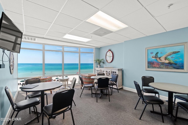 carpeted dining area with a paneled ceiling, a water view, and a view of the beach