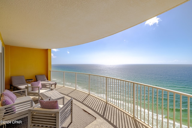 balcony with a view of the beach, an outdoor living space, and a water view