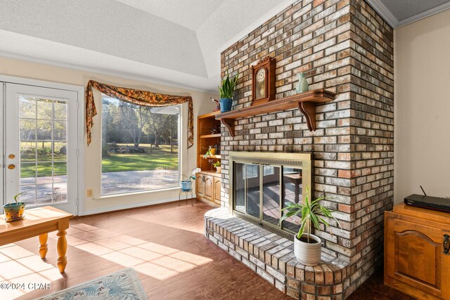 living room with a brick fireplace, crown molding, a textured ceiling, lofted ceiling, and hardwood / wood-style flooring