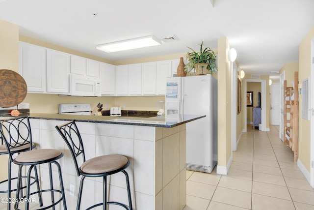 kitchen featuring a breakfast bar, white appliances, dark stone countertops, light tile patterned flooring, and white cabinetry