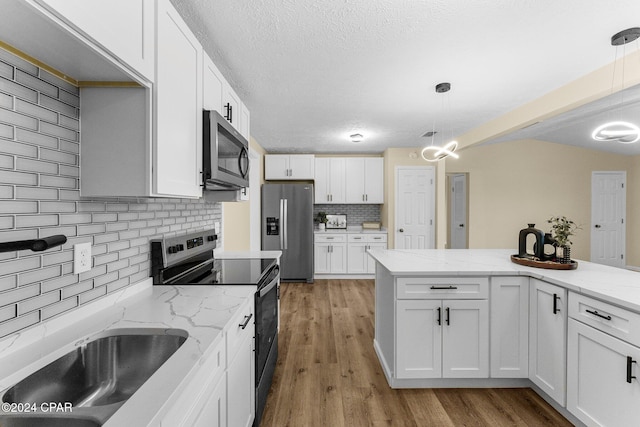 kitchen featuring appliances with stainless steel finishes, backsplash, decorative light fixtures, white cabinets, and light hardwood / wood-style floors