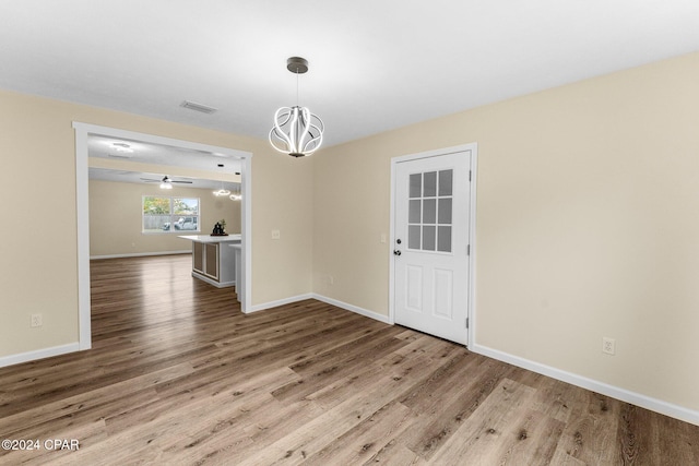 unfurnished dining area with ceiling fan with notable chandelier and wood-type flooring