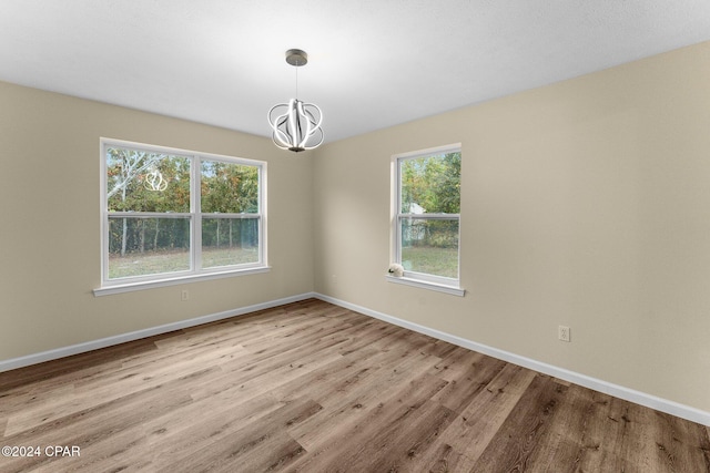 empty room with plenty of natural light, light hardwood / wood-style floors, and a notable chandelier