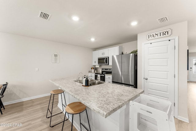 kitchen featuring light wood-type flooring, stainless steel appliances, a kitchen island with sink, sink, and white cabinetry