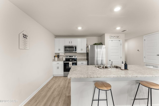 kitchen with a breakfast bar, sink, light wood-type flooring, white cabinetry, and stainless steel appliances