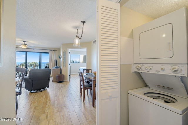 laundry room with a textured ceiling, light wood-style flooring, stacked washer and dryer, laundry area, and visible vents