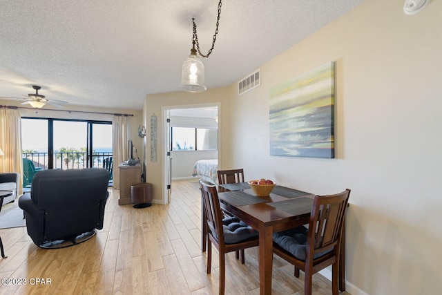 dining space featuring light wood-type flooring, baseboards, visible vents, and a textured ceiling