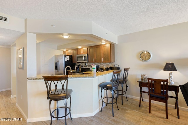 kitchen with a peninsula, brown cabinetry, visible vents, and stainless steel appliances