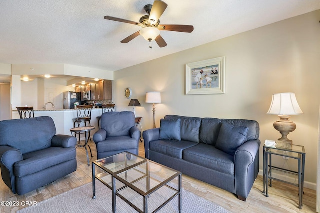 living area featuring a textured ceiling, light wood finished floors, a ceiling fan, and baseboards