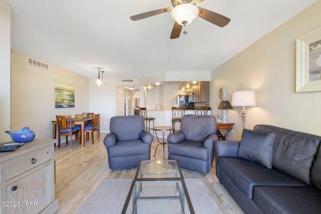 living area featuring light wood-type flooring, visible vents, and a ceiling fan