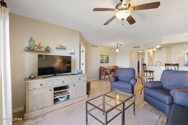 living area featuring baseboards, a ceiling fan, visible vents, and light wood-style floors