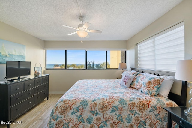 bedroom with a textured ceiling, multiple windows, a ceiling fan, and light wood-style floors