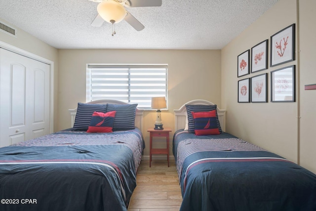 bedroom with a textured ceiling, wood finished floors, visible vents, and a ceiling fan