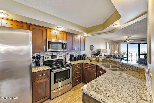 kitchen with light wood finished floors, backsplash, appliances with stainless steel finishes, a sink, and a peninsula