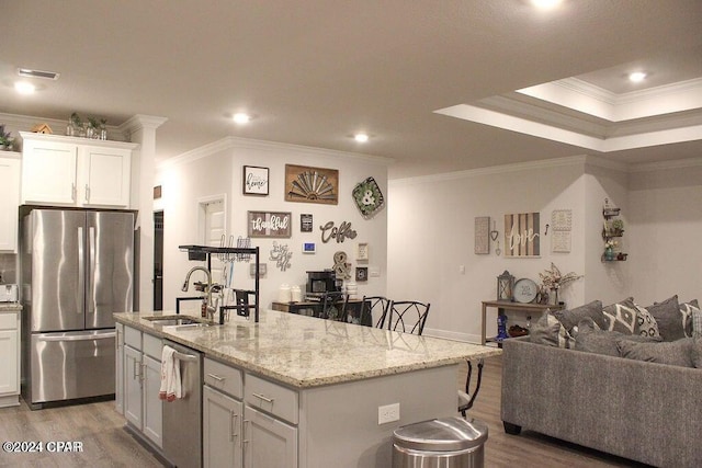 kitchen with a breakfast bar, a center island with sink, ornamental molding, appliances with stainless steel finishes, and white cabinetry