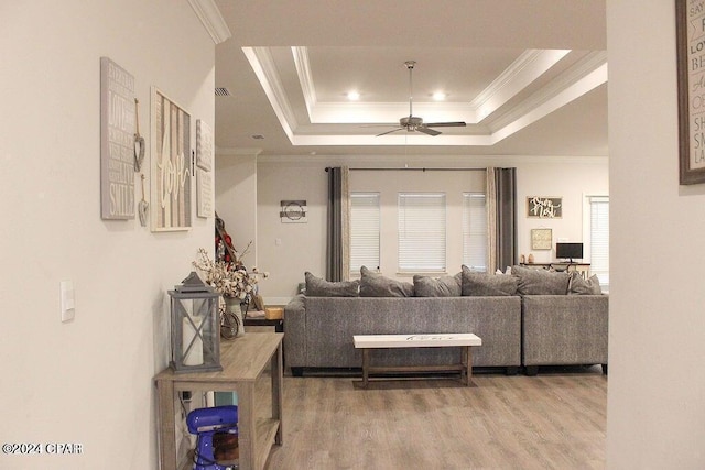 living room with ceiling fan, wood-type flooring, ornamental molding, and a tray ceiling