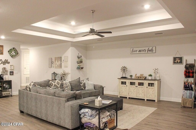 living room featuring a tray ceiling, ceiling fan, hardwood / wood-style floors, and ornamental molding