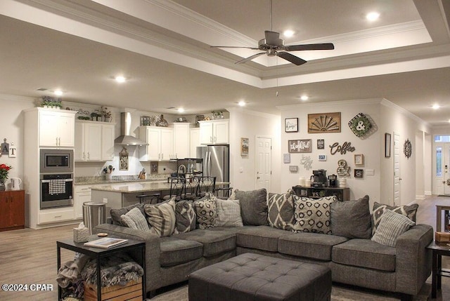 living room featuring light wood-type flooring, a tray ceiling, ceiling fan, and crown molding