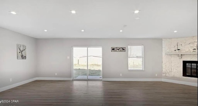 unfurnished living room featuring dark wood-type flooring and a stone fireplace