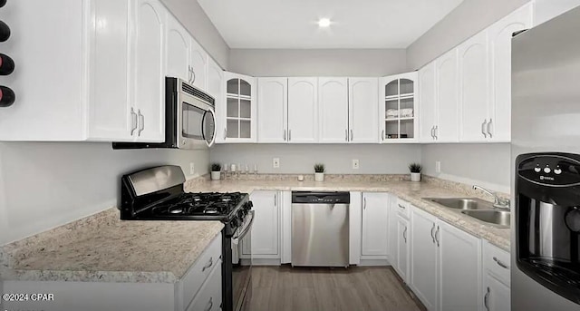 kitchen with stainless steel appliances, sink, light stone counters, white cabinets, and dark hardwood / wood-style flooring