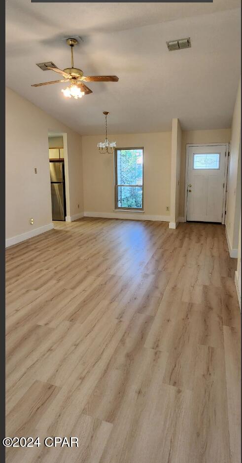 unfurnished living room featuring a wealth of natural light, lofted ceiling, ceiling fan with notable chandelier, and light wood-type flooring