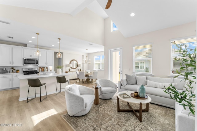 living room with sink, light hardwood / wood-style flooring, ceiling fan with notable chandelier, and high vaulted ceiling