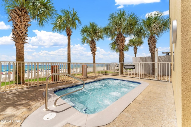 view of swimming pool with a water view, a hot tub, and a beach view