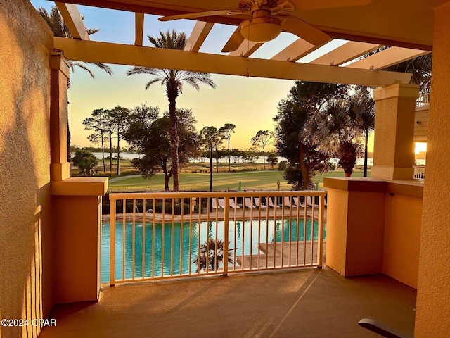 pool at dusk featuring a water view and ceiling fan