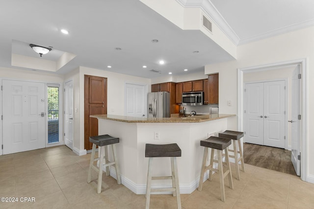 kitchen with crown molding, stainless steel appliances, a kitchen bar, and light stone counters