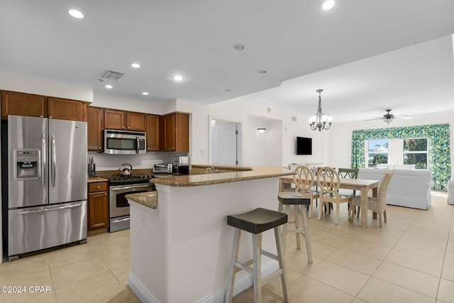 kitchen with hanging light fixtures, a breakfast bar, dark stone counters, ceiling fan with notable chandelier, and stainless steel appliances